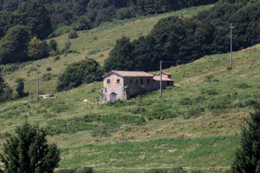 Terk edilmiş gri bir ev uzak bir dağdan görünen bir dağın yamacında virajlı bir yolun kenarındaki bir tarlada