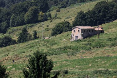 Terk edilmiş gri bir ev uzak bir dağdan görünen bir dağın yamacında virajlı bir yolun kenarındaki bir tarlada