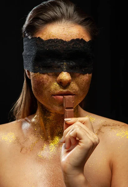 Donna sexy con trucco in oro e maschera di pizzo, mangiare cioccolato — Foto Stock