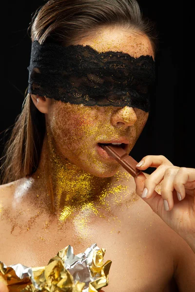 Sexy woman with gold makeup and lace mask, eating chocolate — Stock Photo, Image