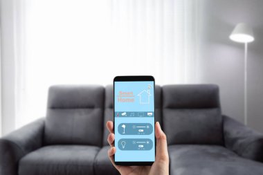 Kadın el ele tutuşan cep telefonu oturma odası arka planına sahip aydınlatma kontrol panelinde akıllı ev uygulaması ekranını gösteriyor