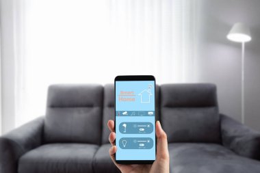Kadın el ele tutuşan cep telefonu oturma odası arka planına sahip aydınlatma kontrol panelinde akıllı ev uygulaması ekranını gösteriyor