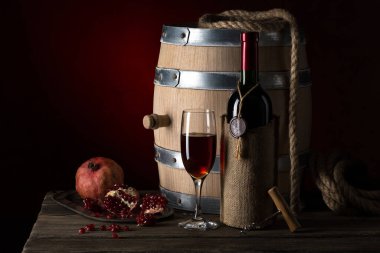 Eski bir şişe ve bardakta nar şarabı, meşe fıçısı ve olgun nar meyveleriyle eski, durgun bir hayat..