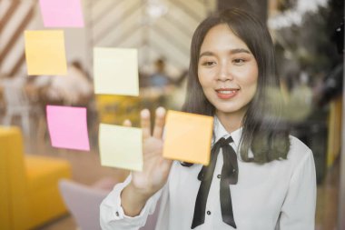 İş kadını kâğıt çubuklara not alıyor. Kadın fikri paylaşmak için post it notlarını kullanır.