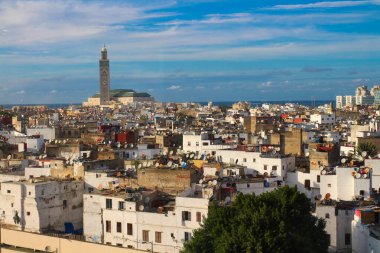 Casablanca evlerinin çatılarının üst manzarasında birçok uydu anteni ve Hassan YI Camii 'nin arkasında bulutlu mavi bir gökyüzü var. Fas.