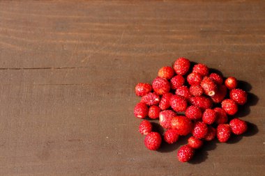 Koyu kahverengi ahşap arka planda olgun, taze, vahşi çilekler..