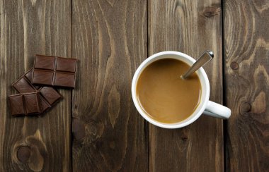 Koyu ahşap arka planda bir fincan kahve ve bir parça çikolata. Üst görünüm