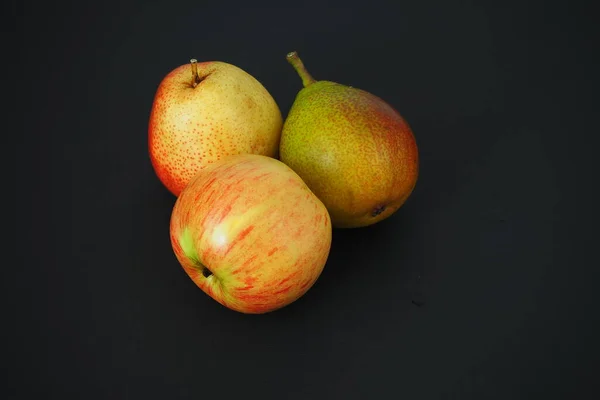 Fruta madura sobre um fundo preto. Duas belas peras e uma maçã. — Fotografia de Stock