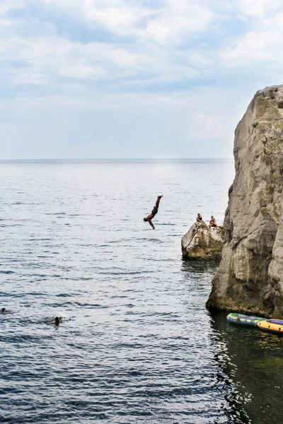 Un hombre se sumerge desde un acantilado en el agua . — Foto de Stock