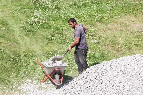 Trabajador carga piedra triturada en una carretilla . — Foto de Stock