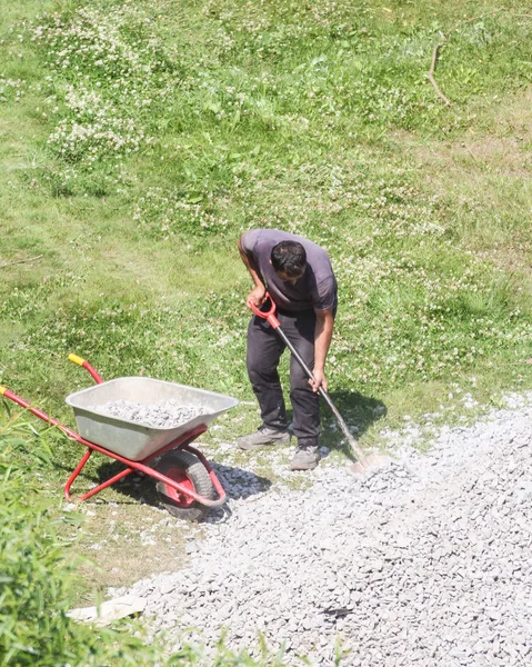 Trabajador con una pala carga piedra triturada en una carretilla . — Foto de Stock
