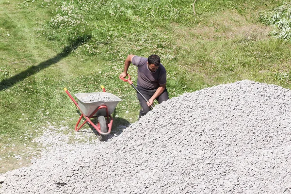 Trabajador con una carretilla cerca de un montón de escombros . — Foto de Stock