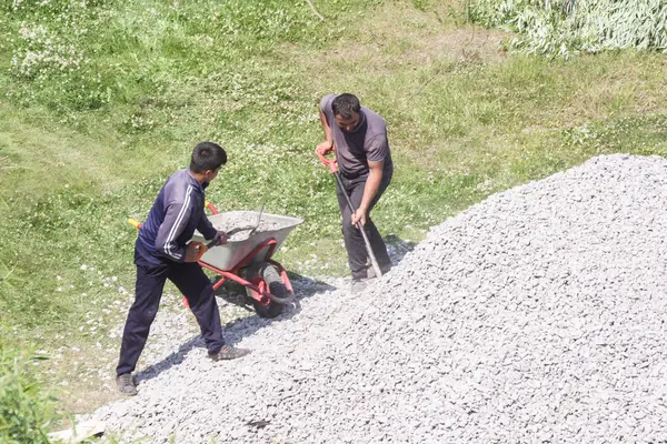 Trabajadores cargan piedra triturada en una carretilla . — Foto de Stock