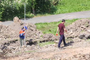 Bir hendek içinde bir ölçme çubuğu ile işçi.