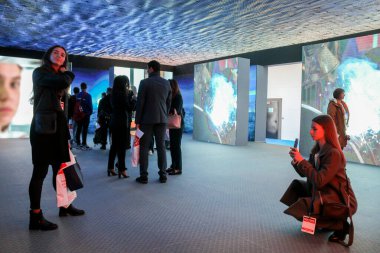 Monitörlerdeki videolardan bir grup insan.