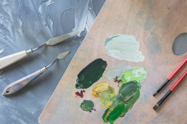 Fırçalar, palet bıçakları ve gri arkaplan boyalı bir palet.