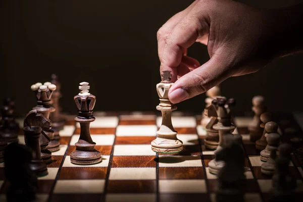 Рука людини тримає чорне проти білих королівських шахових фігур на шахах — стокове фото