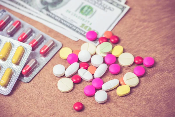 Molti colore di pillole e dollari banconota su sfondo di legno — Foto Stock