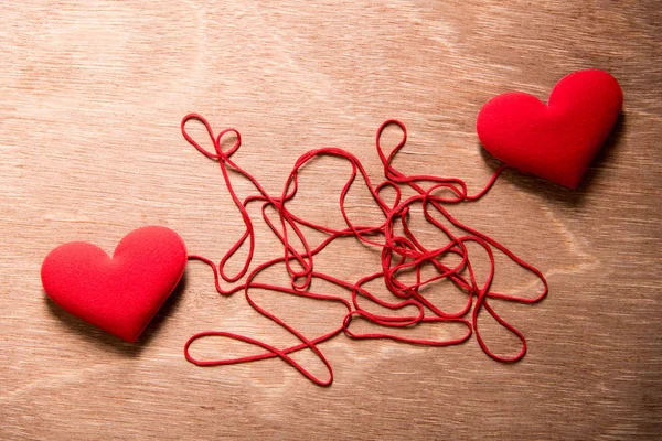 Två röda hjärtan och komplexa röda strängen ansluta tillsammans på trä ba — Stockfoto