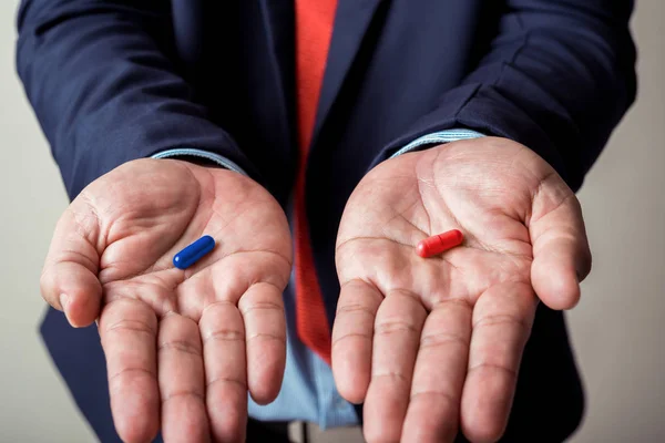 Бізнесмен дає синьо-червону таблетку в руці, виберіть спосіб або — стокове фото