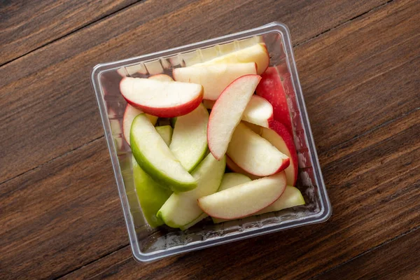 green and red apples are cut into pieces and placed in a clear box ready to be eaten , food delivery concept