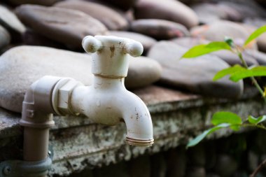 Bahçede plastik musluk ve arka planda bulanık taşlar.