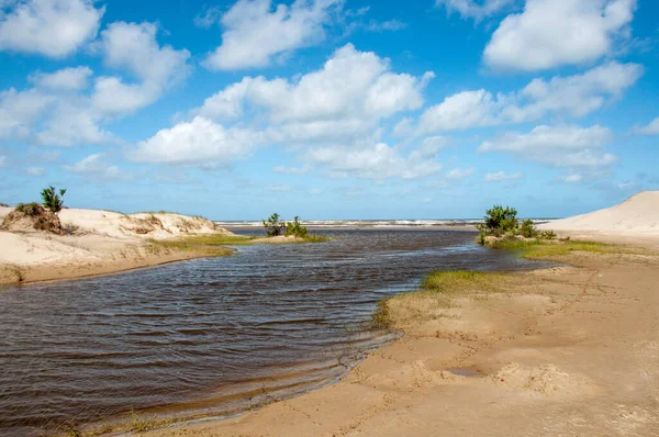 Kum tepelerinin arasından akan nehir mavi gökyüzü ve Cassino, Rio Grande do Sul 'daki bulutlarla denize akıyor. 