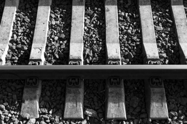 Demiryolu raylarının siyah-beyaz bir fotoğrafı, desenli beton desteklerin üzerine düzgünce yerleştirilmiş, küçük molozlara batırılmış, ilginç bir şablon oluşturuyor. Demiryolunun bir parçası, yakın plan, arka plan..