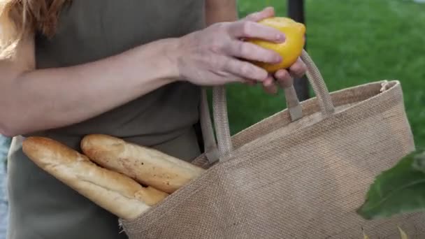 Молодая женщина кладет лимоны в сумку с багетами — стоковое видео