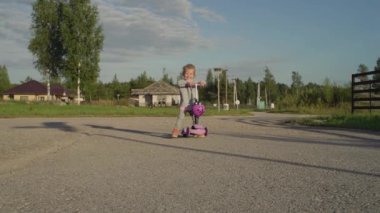 Köyde gün batımında, açık havada. Genç bir kız scooter kullanıyor..