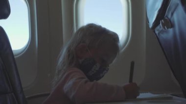 Çocuk, COVID-19 salgını sırasında bir uçağa maske takarak biner ve bir albüm çizer.