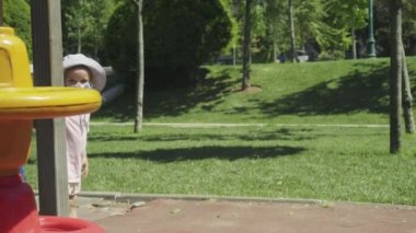 Bir çocuk salgın sırasında çocuk parkında maske takıyor..