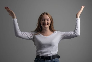 Neşeli, genç bir kadın gündelik giysiler içinde pozitif haberler ya da doğum günü hediyesi, neşeli ve büyüleyici bir gülümsemeyle gözlerini kapatıyor. Eller koyu gri arkaplanda, stüdyo çekimi