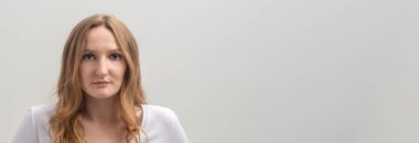 Beyaz tişört giyen, beyaz tişörtlü, sakince ve dikkatlice kameraya bakan, gri arka planda, uzun altın saçlar, kopya alanı, afiş...