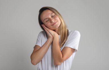 Gülümseyen genç kadın gözleri kapalı uyuyor. Bin yıllık sarışın bir kadının el ele tutuşup uykulu bir şekilde gri arka planda uyuyormuş gibi yaptığı bir resim.