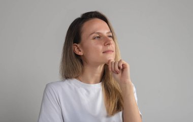 Kafası karışmış, güvenilmez yüzlü, gri stüdyo duvarında izole edilmiş, kuşkulu, kuşkulu, kameraya bakan, şüpheli, sarışın, beyaz kadın.