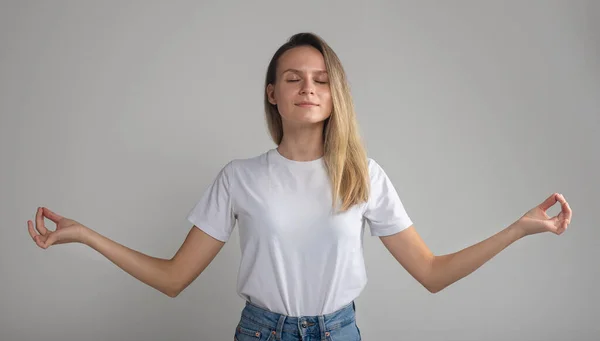 Il mio corpo e 'fortezza. Calma giovane donna europea alla moda con i capelli biondi, in piedi con gli occhi chiusi e l'espressione rilassata, diffondendo le mani in gesto zen — Foto Stock