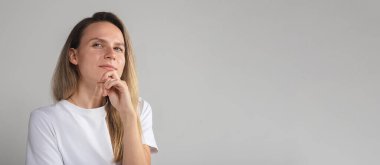 Şaşırmış, kafası karışmış, güvenilmez yüzlü, gri stüdyo duvarında soyutlanmış, güvenilmez, şüpheli kız kameraya şüpheli bir şekilde bakıyor.