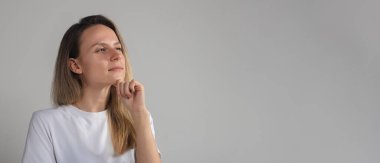 Şaşırmış, kafası karışmış, güvenilmez yüzlü, gri stüdyo duvarında soyutlanmış, güvenilmez, şüpheli kız kameraya şüpheli bir şekilde bakıyor.