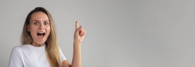 Mutlu, şaşkın, neşeli, genç bir kadın işaret parmağını kaldırmış bir fikirle çıkageliyor. Gri arkaplanda izole edilmiş kadın
