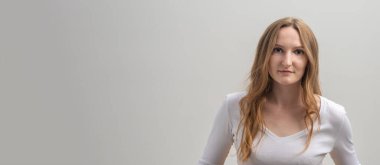 Beyaz tişört giyen, beyaz tişörtlü, sakince ve dikkatlice kameraya bakan, gri arka planda, uzun altın saçlar, kopya alanı, afiş...