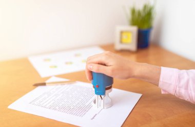 Kadın elini kapar kontrat imzalarken ve imzalarken mavi pulu tutar, yatırım yapar, sigorta yaptırır, vasiyet tutar, ofis masasını kapatır.