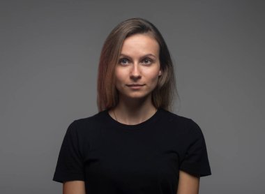 Sakin ciddi bir kadın siyah tişörtlü koyu bir arka plana bakıyor.