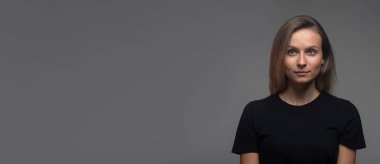 Sakin ciddi bir kadın siyah tişörtlü, fotokopi odası, afiş ile koyu arkaplana bakıyor.