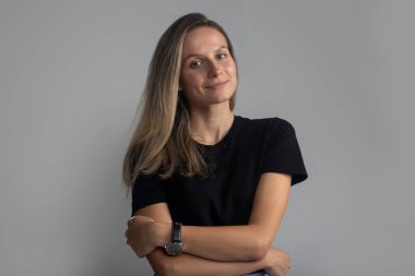 Güzel, genç, güler yüzlü ve kendine güvenen bir kadın portresi sakince kameraya bakıyor. Stüdyo çekimi, gri arkaplanda izole edilmiş.