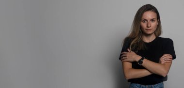 Gri stüdyonun arka planında kameraya bakan, kendine sarılan, göğsünde çapraz kollar olan, yalnız hisseden, zorbalıktan ya da tacizden muzdarip bir kadın.