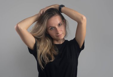 Sakin, dost canlısı, elleri başının üstünde gri arka plandaki kameraya bakan bir kız.