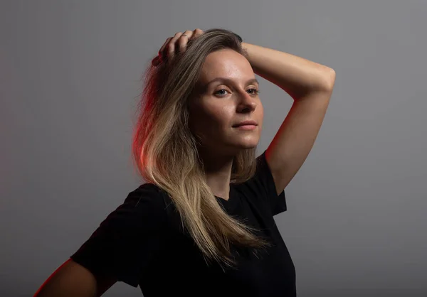 Pretty young arrogant woman in black t-shirt posing over dark background with hand over head, red light