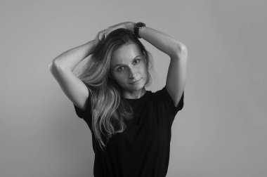 Taze, sakin, arkadaş canlısı, elleri başının üstünde gri arka planda kameraya bakan bir kız.