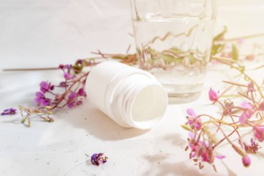 Bir kavanoz hap, bir bardak su ve bitkiler beyaz bir arka planda haplar yerine sağlık ve şifa kavramı şifalı bitkiler, tıbbi ilaçlar.